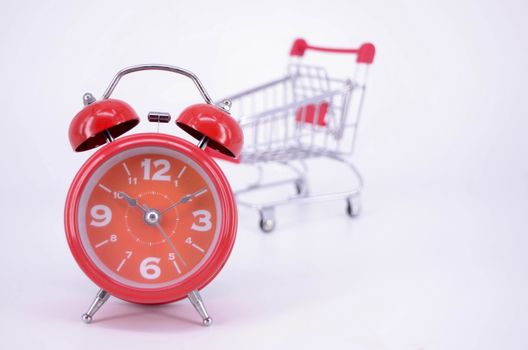 Shopping cart and classic alarm clock on white background. Sale time buy mall market shop consumer concept. Selective focus.