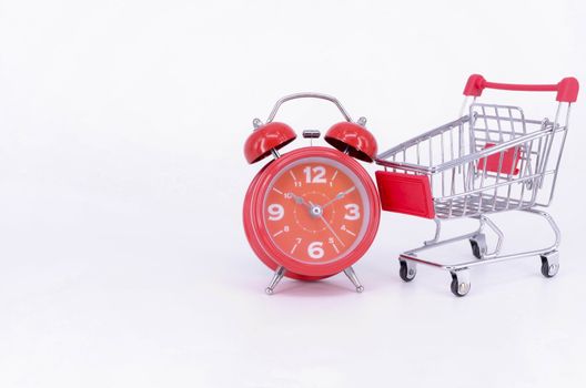 Shopping cart and classic alarm clock on white background. Sale time buy mall market shop consumer concept. Selective focus.