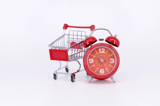 Shopping cart and classic alarm clock on white background. Sale time buy mall market shop consumer concept. Selective focus.