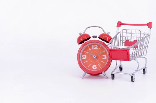 Shopping cart and classic alarm clock on white background. Sale time buy mall market shop consumer concept. Selective focus.