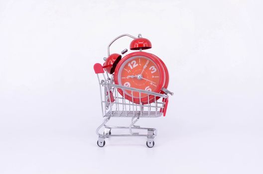 Shopping cart and classic alarm clock on white background. Sale time buy mall market shop consumer concept. Selective focus.