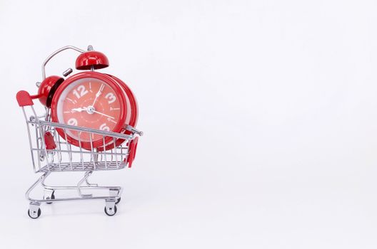 Shopping cart and classic alarm clock on white background. Sale time buy mall market shop consumer concept. Selective focus.