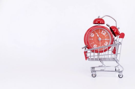 Shopping cart and classic alarm clock on white background. Sale time buy mall market shop consumer concept. Selective focus.