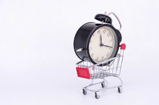 Shopping cart and classic alarm clock on white background. Sale time buy mall market shop consumer concept. Selective focus.