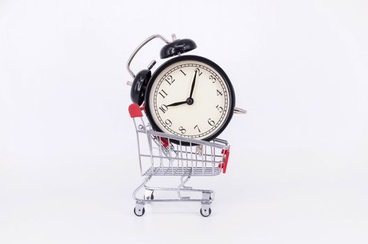 Shopping cart and classic alarm clock on white background. Sale time buy mall market shop consumer concept. Selective focus.