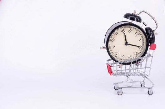 Shopping cart and classic alarm clock on white background. Sale time buy mall market shop consumer concept. Selective focus.