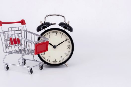 Shopping cart and classic alarm clock on white background. Sale time buy mall market shop consumer concept. Selective focus.