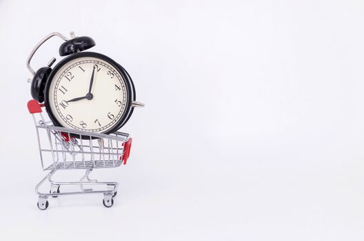 Shopping cart and classic alarm clock on white background. Sale time buy mall market shop consumer concept. Selective focus.