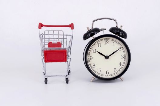 Shopping cart and classic alarm clock on white background. Sale time buy mall market shop consumer concept. Selective focus.