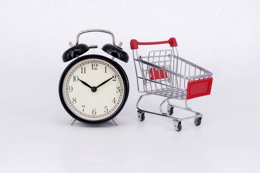 Shopping cart and classic alarm clock on white background. Sale time buy mall market shop consumer concept. Selective focus.