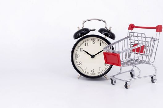 Shopping cart and classic alarm clock on white background. Sale time buy mall market shop consumer concept. Selective focus.