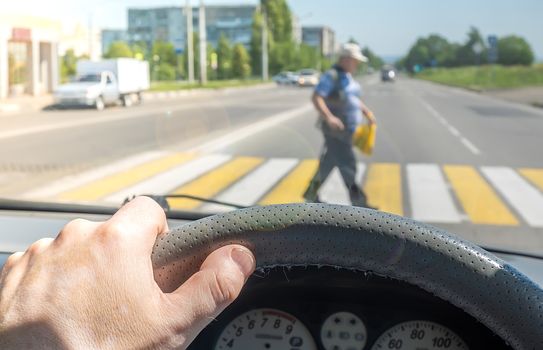 view from the car, the man's hand on the steering wheel of the car, located opposite the pedestrian crossing and pedestrians crossing the road