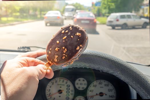 the driver holds the ice cream in his hand while driving the car on the road