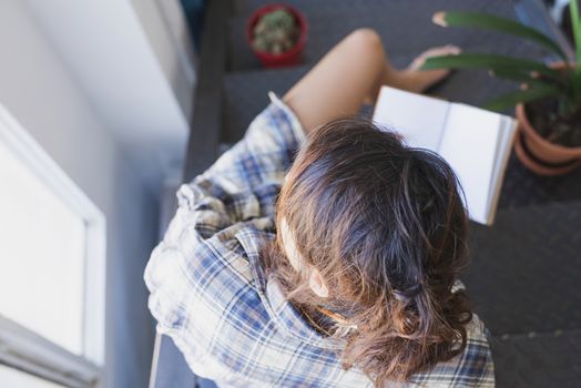 Young woman with a ponytail sitting on a staircase while using a notebook next to a window