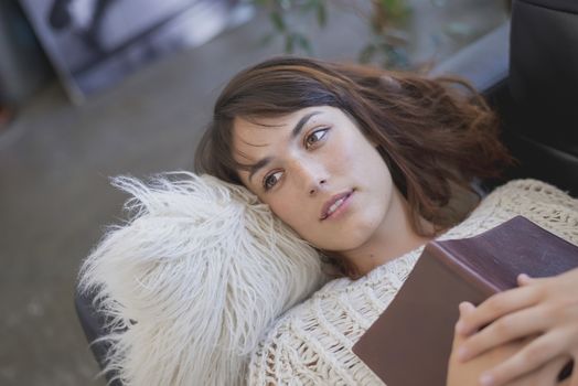Young tired young woman lying on a sofa with a book