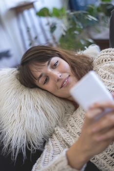 Portrait of smiling nice woman using cellphone while lying on sofa