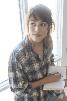 Young woman with a ponytail sitting on a staircase while using a notebook next to a window