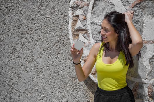Attractive young woman near ancient wall using a smartphone in a sunny summer day