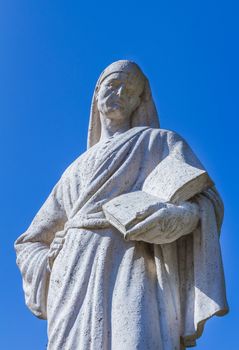 Statue of Poet Dante Alighieri with blue sky in the background. The writer has a book in his hand.