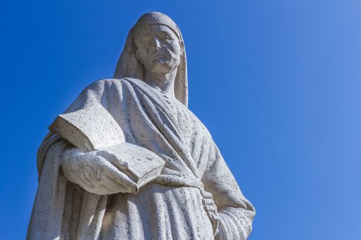 Statue of Poet Dante Alighieri with blue sky in the background. The writer has a book in his hand.