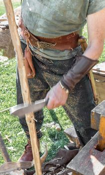Craftsman with traditional medieval clothes manufactures a wooden arch with ancient method. Close up. Shallow deep of field.