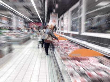 People chooses meat in the supermarket. Radial/motion blur.