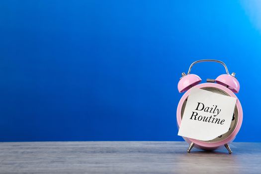 Alarm clock and daily routine words on sticker note paper on blue background