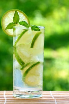 Cocktail mojito with lime and ice cubes on a blurred background.