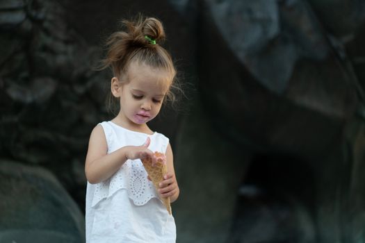 Little caucasian girl 3 years old eats ice cream closeup portrait. Summertime. Childhood Child with frozen dessert in hand walking outdoor. Close up portrait european girl witn ice-cream.