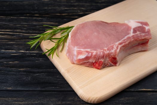 Top view of one pieces raw pork chop steaks with rosemary on a cutting board. Wooden table.
