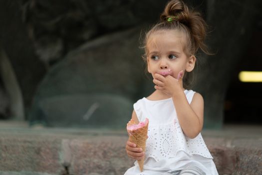 Little caucasian girl 3 years old eats ice cream closeup portrait. Summertime. Childhood Child with frozen dessert in hand walking outdoor. Close up portrait european girl witn ice-cream.