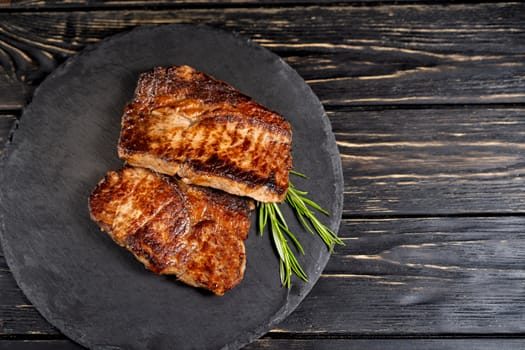 A juicy piece of fried meat lies on a stone plate against a black wooden table. Degree of roasting well done. Food concept with copy space