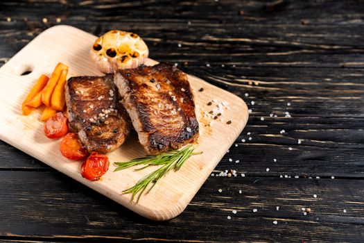 A juicy piece of fried meat with grilled cherry tomatoes garlic and carrot lies on a cutting board against a black wooden table. Degree of roasting well done. Food concept with copy space