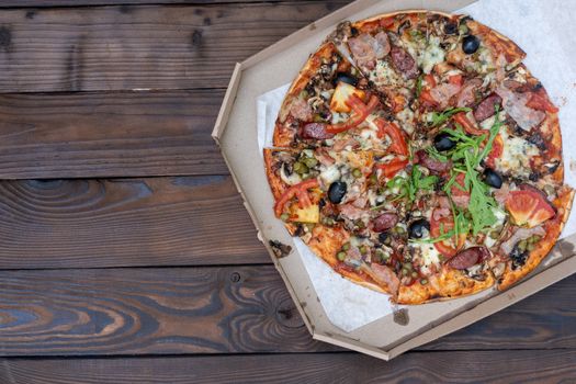 Appetizing pizza with smoked sausages bacon meat tomato cheese arugula cardboard boxes for delivery on black dark background. With copy space for text