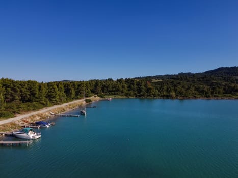 Aerial top view of Glarokavos lagoon at Kassandra Chalkidiki peninsula above shoreline with green plantation & calm blue waters.