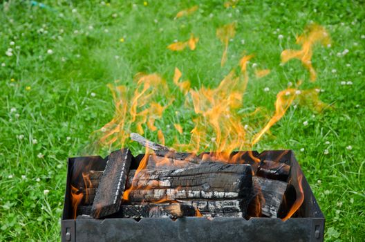 Close up view of the fire tongues in the barbecue on a green garden grass