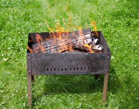 Close up view of the fire tongues in the barbecue on a green garden grass