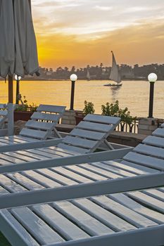 Landscape view of traditional egyptian felluca sailing boat on river Nile at dusk sunset from hotel with sunbeds