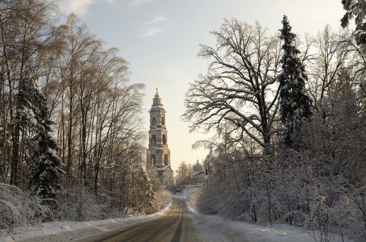 Winter view of the ancient church and bell tower in the Russian village Avdotieno, surrounded by frozen trees