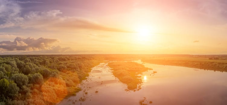 Aerial view to sunset on the river at summer evening with clouds and trees. Water reflection of a sky.