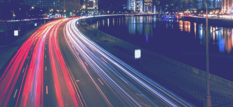 Moving car with blur light through city at night near Moscow river embankment and illuminated Radisson or Ukraine hotel. Moscow, Russia.