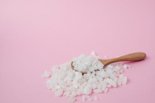 Sea salt in a wooden spoon on pink background for seasoning or preserving food