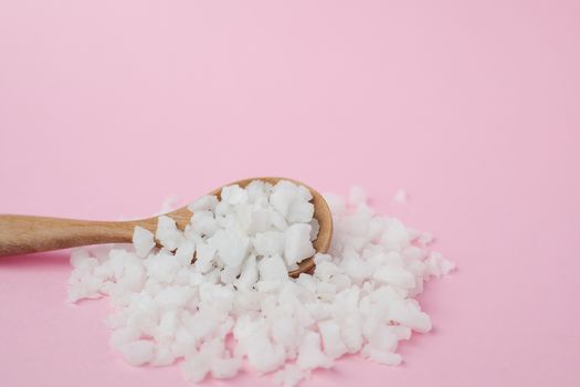 Sea salt in a wooden spoon on pink background for seasoning or preserving food