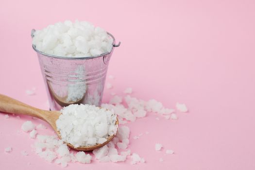 Sea salt in a wooden spoon and full of a tin bucket on pink background for seasoning or preserving food