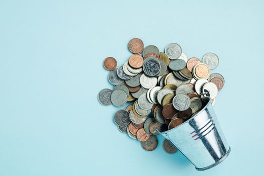 Full of money coins in a tin bucket on blue background for investment, business, finance and saving money concept 