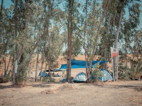 Many dome tents at a camping site near the Eucalyptus trees in Jordan Valley of Israel. Adventure vacation near the Jordan river on a sunny summer day. A sign symbolizing swimming is prohibited.