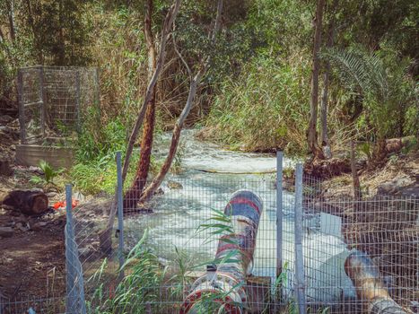 Water flowing from a drainpipe into a small river. In the forest near the Jordan River in Israel. Concept of water abundance or water and nature pollution.