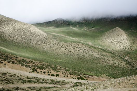 Clouds are moving down to the high mountain green valley along the meandering route from Ghemi to Lo Manthang, Upper Mustang, Nepal