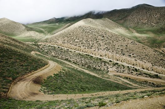 Clouds are moving down to the high mountain green valley along the meandering route from Ghemi to Lo Manthang, Upper Mustang, Nepal