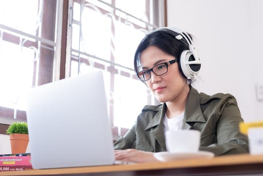 Modern young Asian woman working from home and listening to the music with a white headphones.